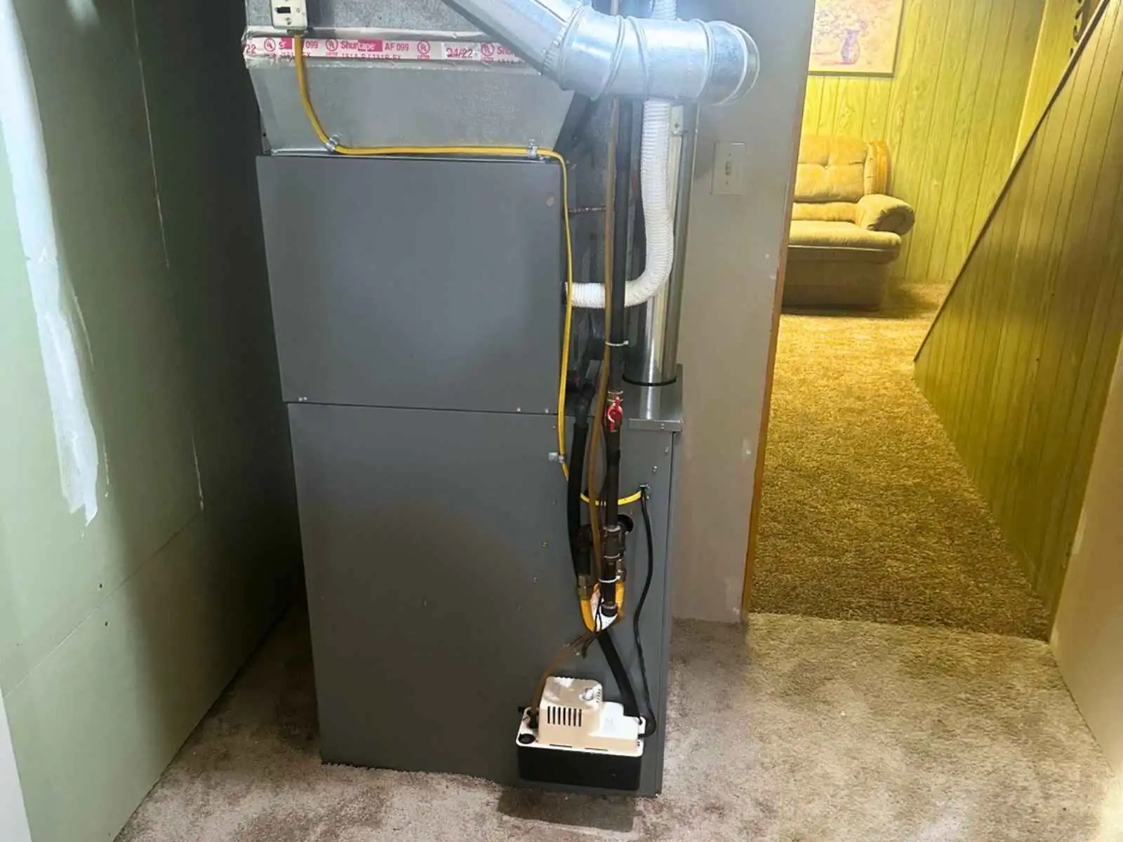 Residential furnace with metal ductwork, gas supply piping, and a condensate pump.
